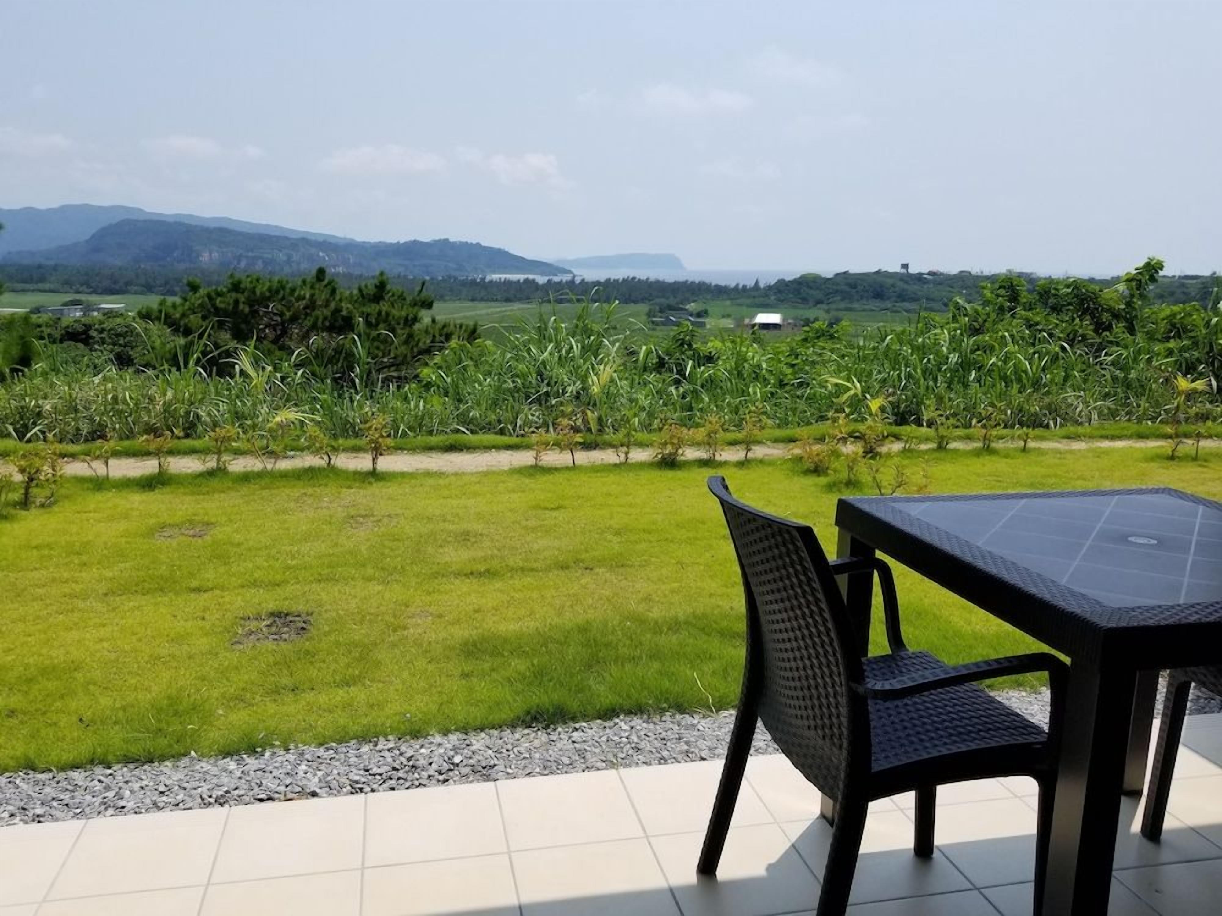 An outdoor patio with a table and chairs, overlooking a grassy field and distant hills.