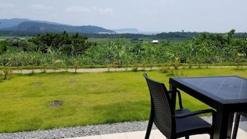 An outdoor patio with a table and chairs, overlooking a grassy field and distant hills.