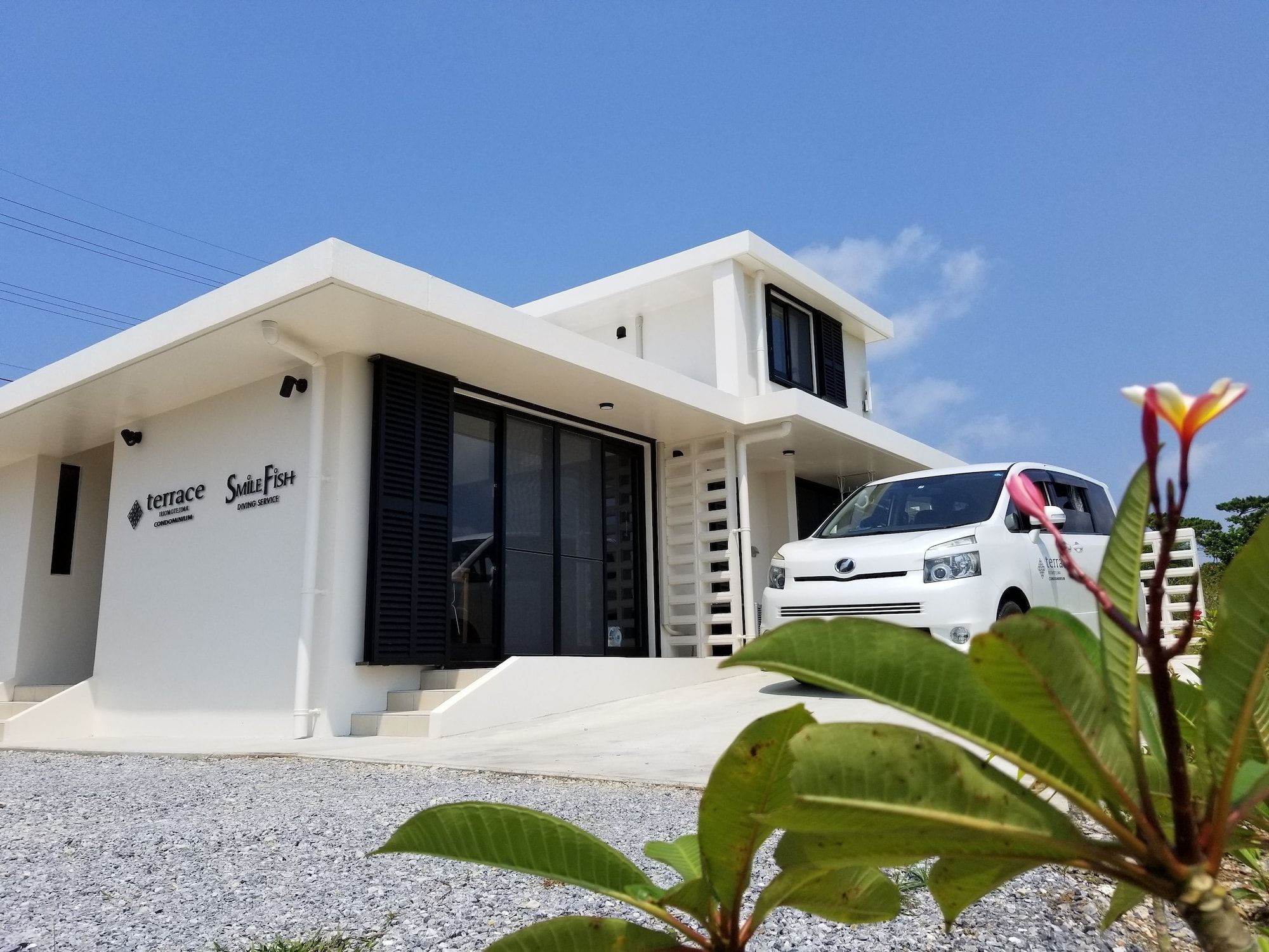 A modern two-story building with a white exterior, a car parked in front, and a sign indicating a terrace and swimming service.