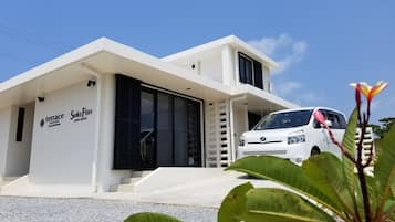 A modern two-story building with a white exterior, a car parked in front, and a sign indicating a terrace and swimming service.