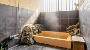 Een badkamer met een houten bad, stenen muren en een raam met tralies.
