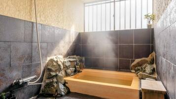 A bathroom with a wooden bathtub, stone walls, and a window with bars.