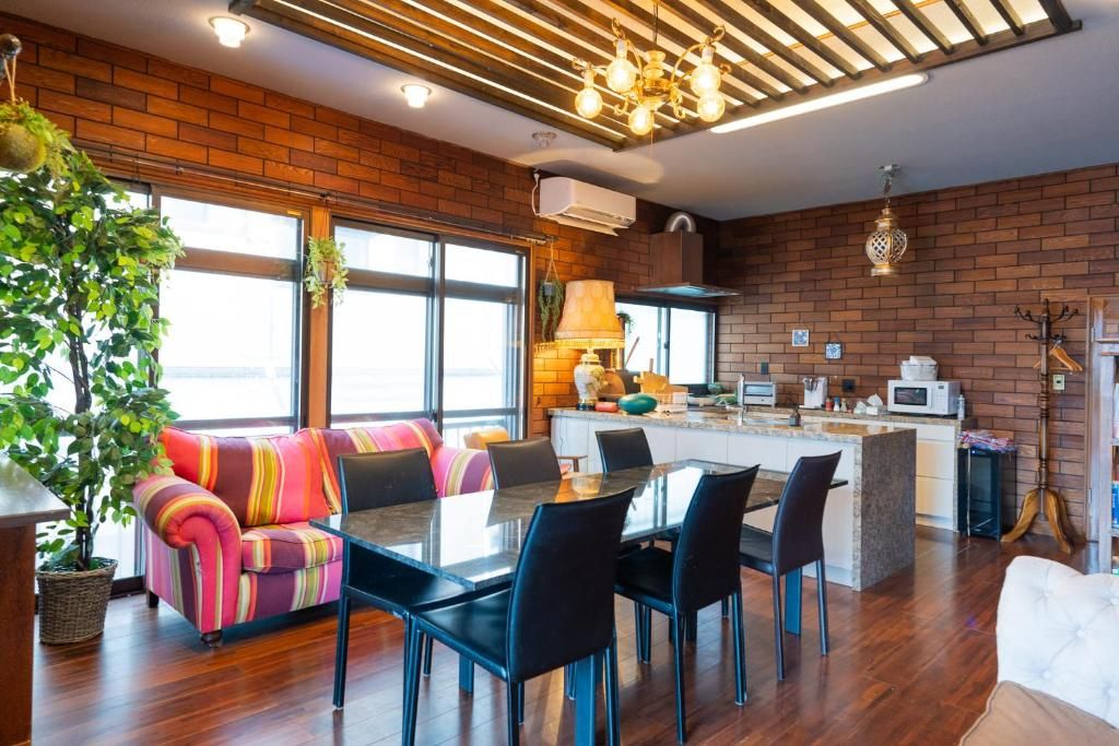 A modern kitchen with a brick wall, a dining area with a glass table and black chairs, and a large window providing natural light.