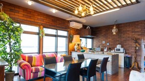 Een moderne keuken met een bakstenen muur, een eethoek met een glazen tafel en zwarte stoelen, en een groot raam dat voor natuurlijk licht zorgt.