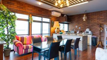 A modern kitchen with a brick wall, a dining area with a glass table and black chairs, and a large window providing natural light.