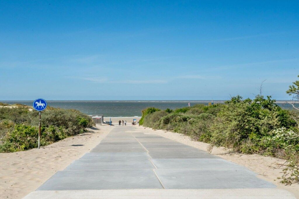 Uma trilha pavimentada leva a uma praia, com vista clara para o oceano.