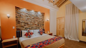 Quarto com cabeceira de parede de tijolos, cama de madeira, duas mesas de cabeceira e uma janela grande com cortinas.