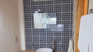 Casa de banho com uma pia branca, espelho e painel de azulejos.