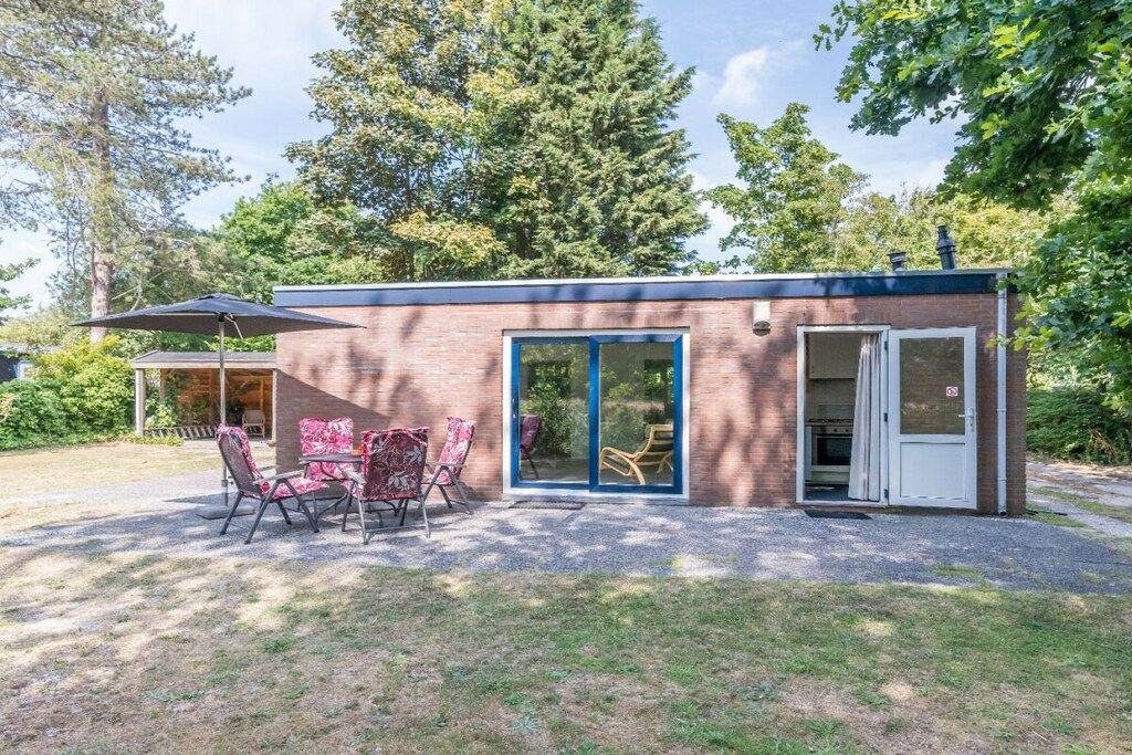 A small brick building with a sliding glass door entrance, a patio with outdoor seating, and a covered area with a table and chairs.
