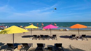Uma praia com espreguiçadeiras, guarda-sóis e um parapente ao fundo.