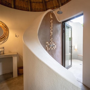 A modern bathroom with a curved wall, a shower, and a glass door leading to an outdoor area. - Nyala Safaris (Hoedspruit)