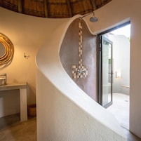 Un baño moderno con una pared curva, una ducha y una puerta de cristal que da a un espacio exterior.