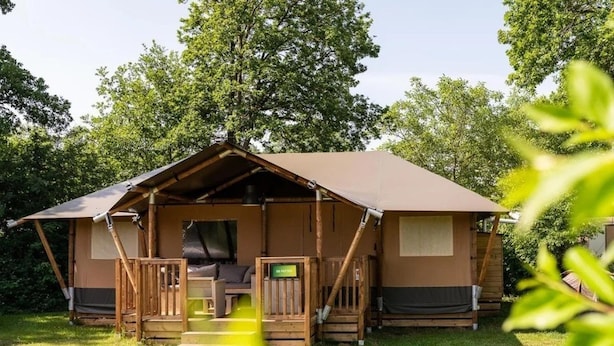 A single-story, A-frame-style cabin with a porch, a bed, and a small table. - Family Lodge With Garden Retreat in Wilsum (Wilsum)