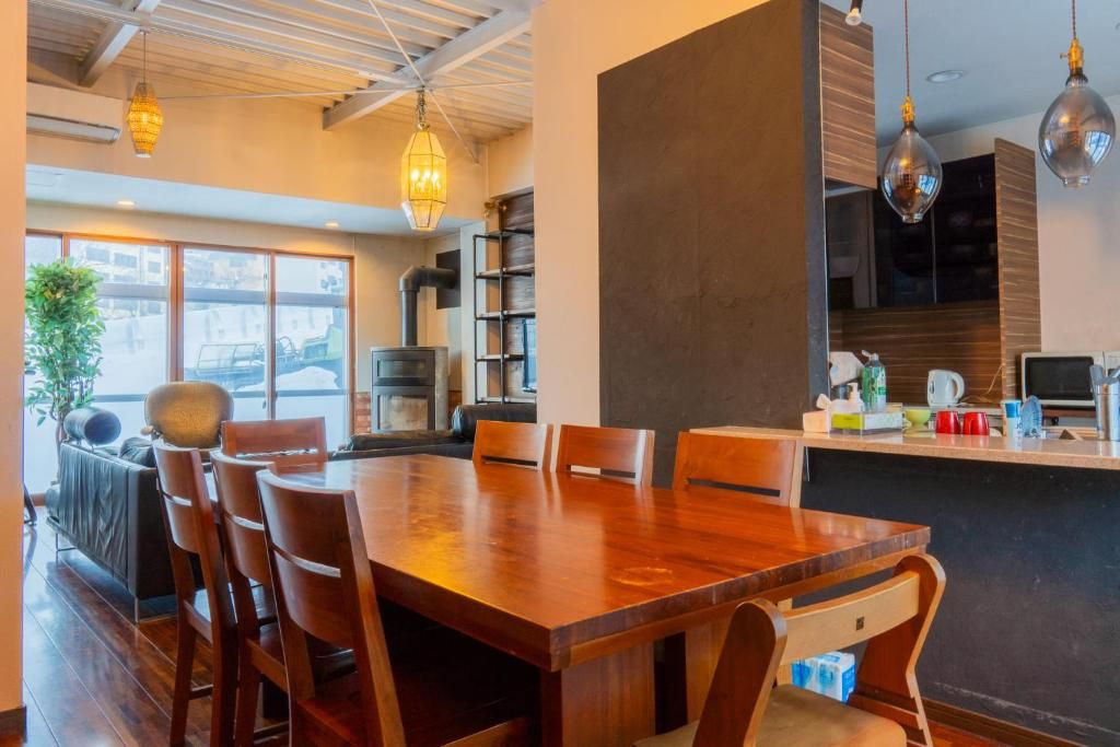 A modern dining area with a wooden table and chairs, a kitchen area with a stove, and pendant lighting.