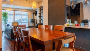 Un'area pranzo moderna con tavolo e sedie in legno, angolo cottura con piano cottura e illuminazione a sospensione.