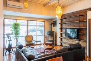 A modern living room with a fireplace, a television, and a large window overlooking a snowy landscape. - Onsen Villa Gensen Two (Minamiuonuma-gun)