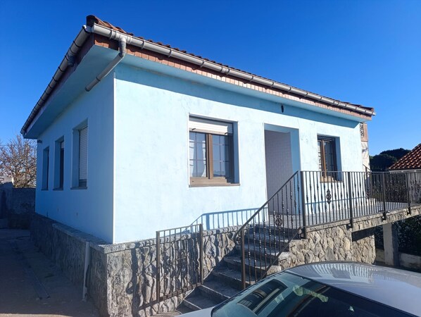 A two-story building with a stone base, a balcony with metal railings, and a car parked in front.