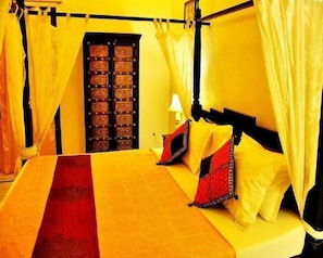 Una cama con dosel, una mesita de noche con lámpara y una puerta con celosía metálica.