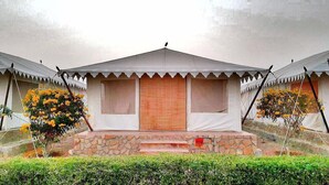 Un edificio con techo a dos aguas y base de piedra, flanqueado por dos árboles con flores amarillas.