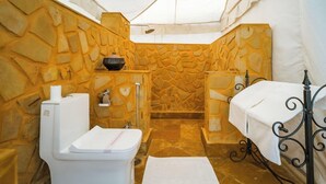Baño compacto con pared de piedra, inodoro, lavabo y una mesita con una toalla.