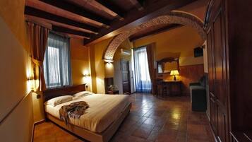 A hotel room with a large bed, a desk, and a chair. There is a window with curtains, a lamp, and a wall-mounted air conditioning unit.