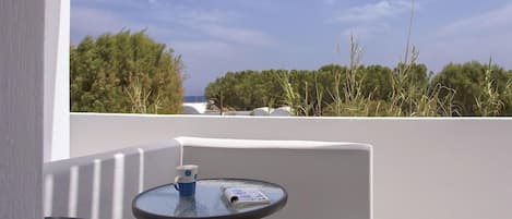 Un balcón con mesa y sillas, con vista a una zona costera con vegetación y cielo despejado.