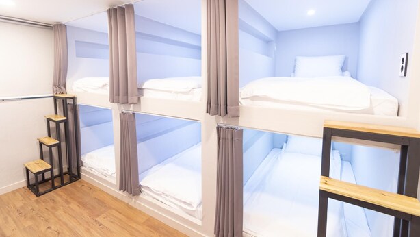 Ein Zimmer mit Etagenbetten, einem kleinen Holzschemel und einer weißen Wand.