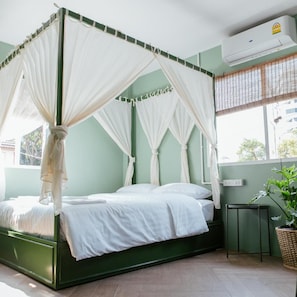 A four-poster canopy bed with white bedding, a green bed frame, and a small bedside table with a plant. - Malarer Boutique Hostel (Chonburi)