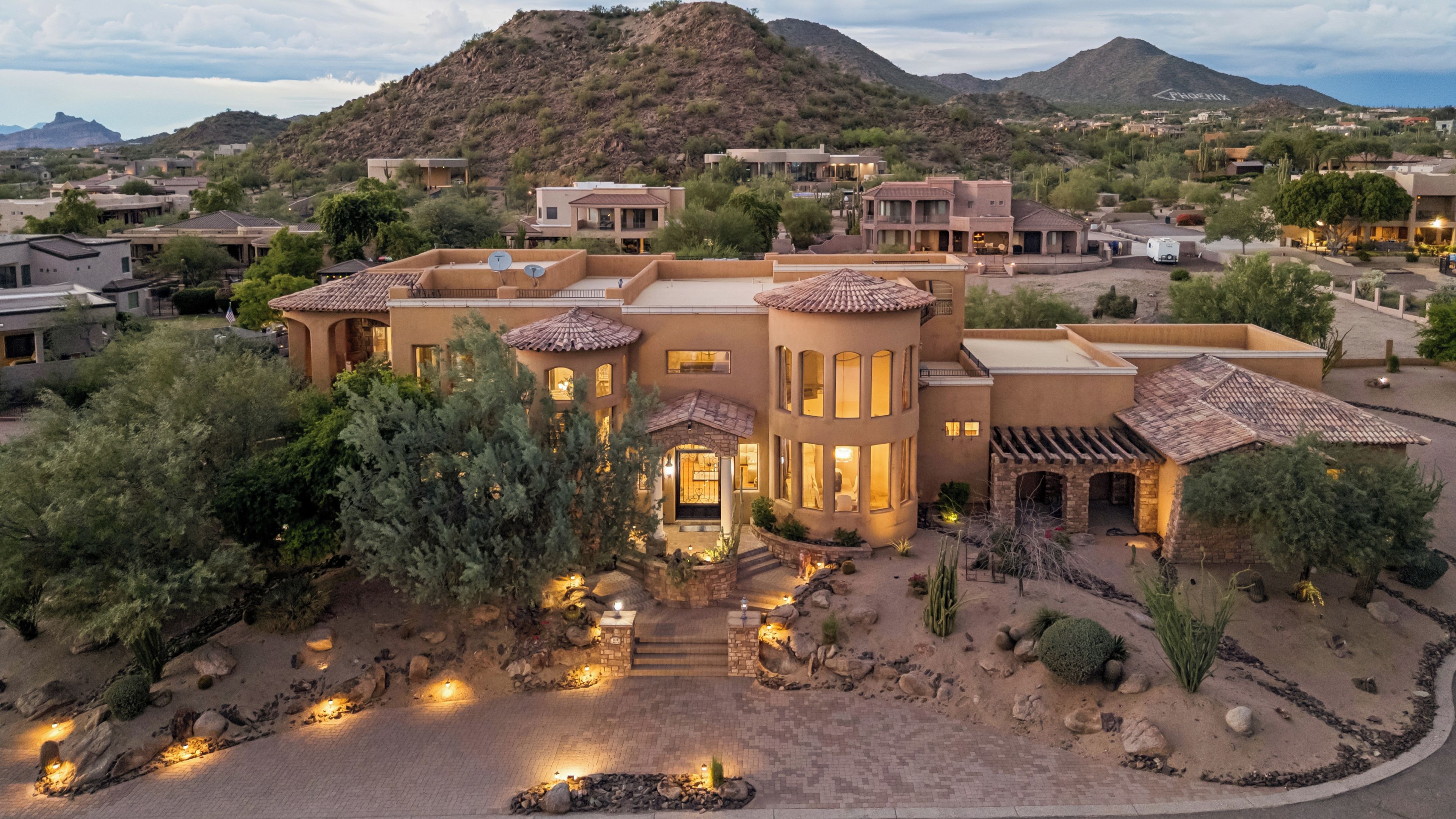A large, multi-story building with a courtyard, surrounded by desert vegetation and mountains.