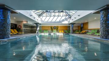 Una piscina interna con soffitto a lucernari, pilastri in pietra e poltrone relax.