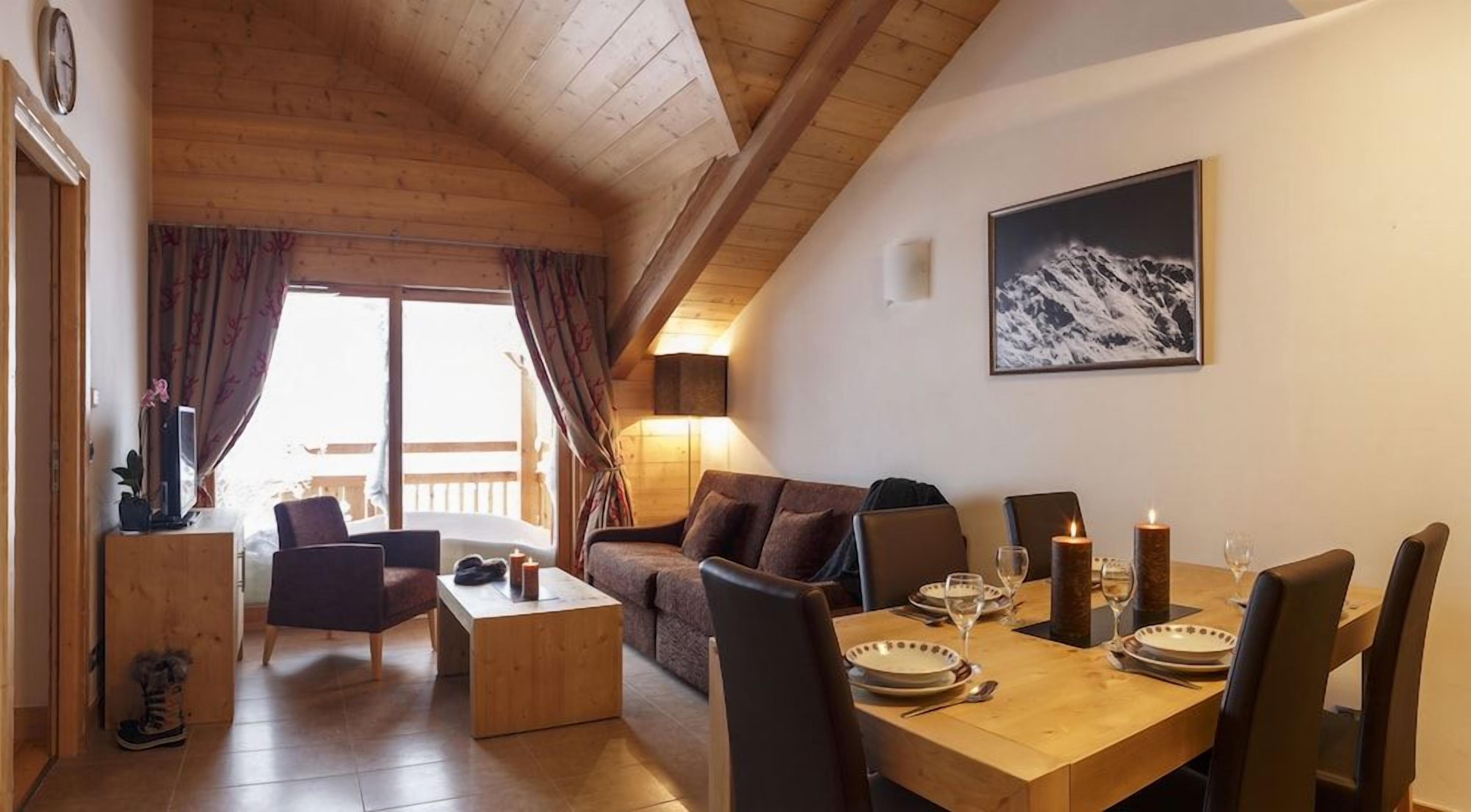 Una stanza accogliente con soffitto in legno, un tavolo da pranzo apparecchiato per due e un divano.