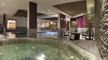 Una hall d'hotel con una grande piscina interna, un'area salotto e un muro in pietra.