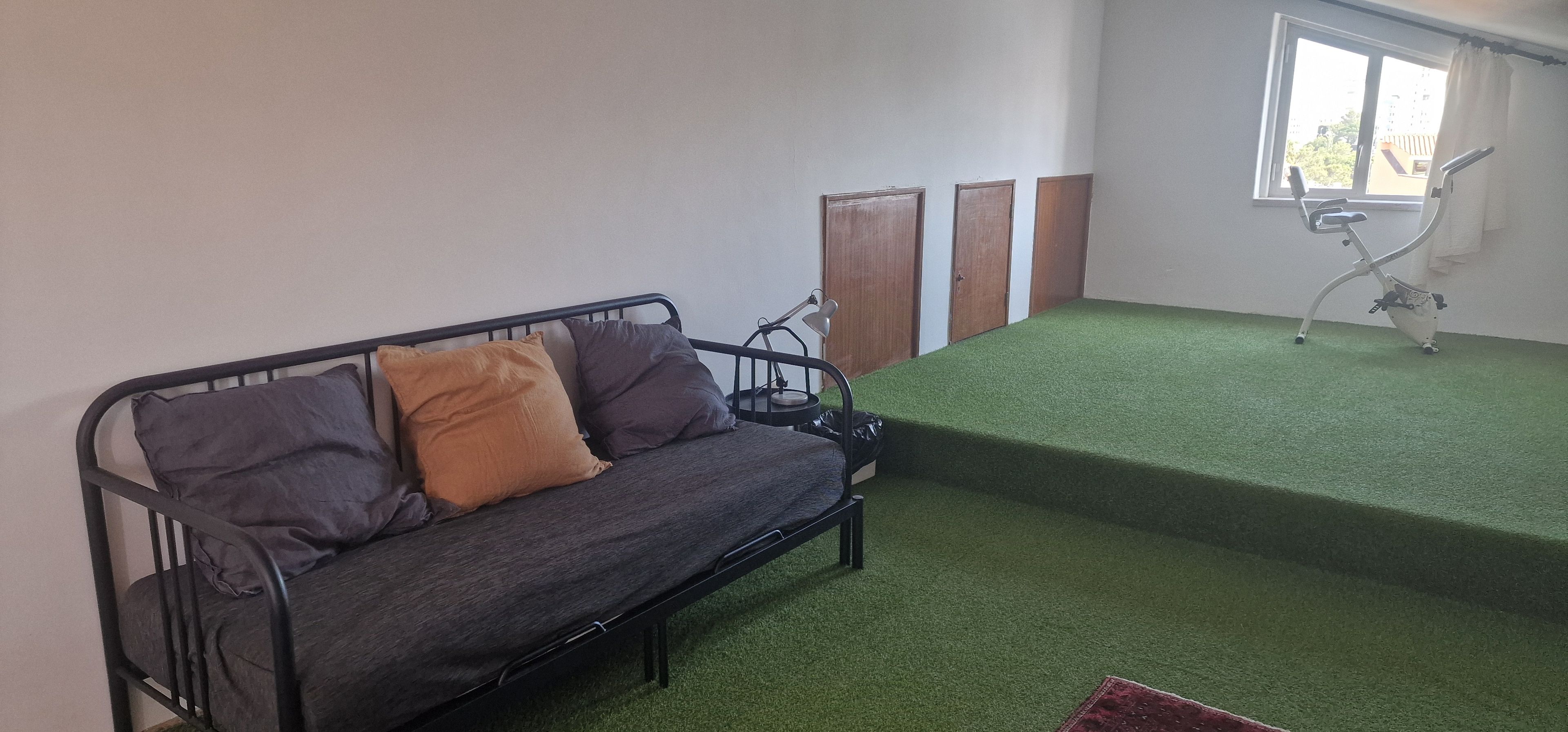 A room with a sofa, a small table, a lamp, a window, and a green carpet.