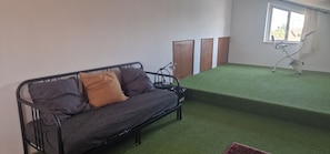 A room with a sofa, a small table, a lamp, a window, and a green carpet.