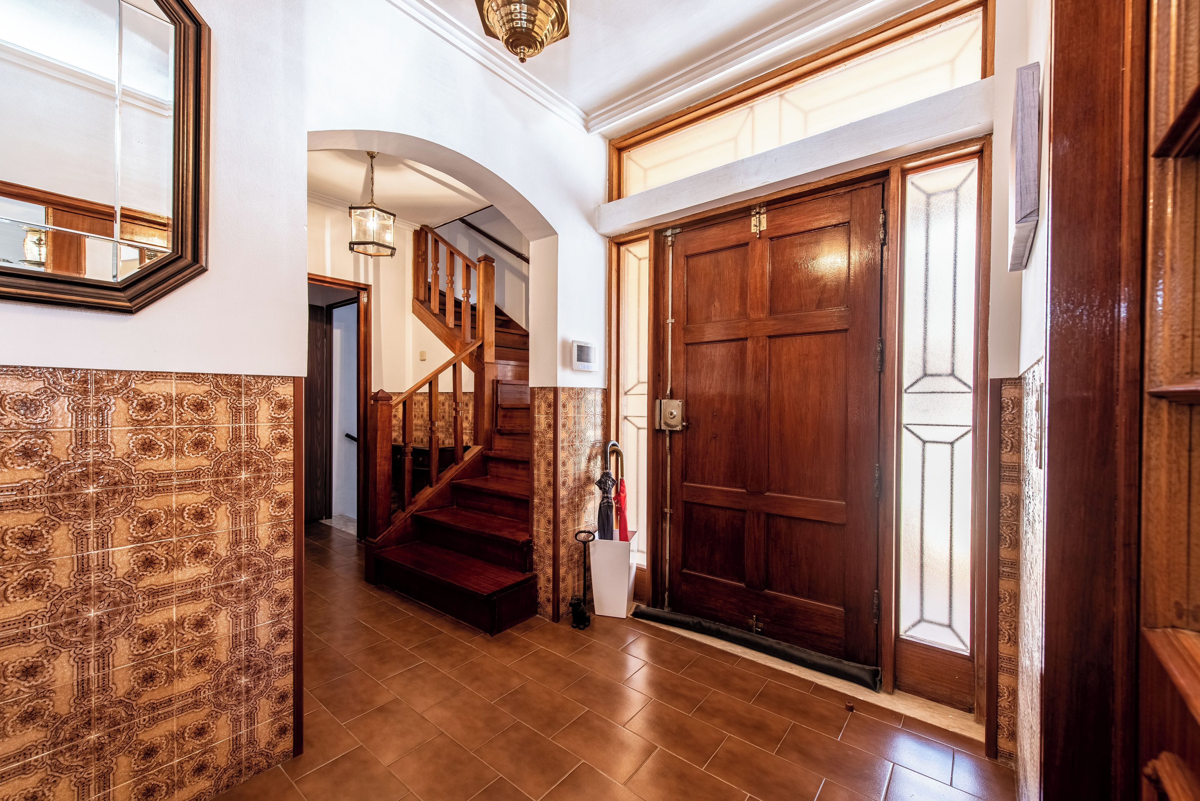 A grand hallway with a wooden staircase, a large wooden door with glass panels, and a patterned wall.