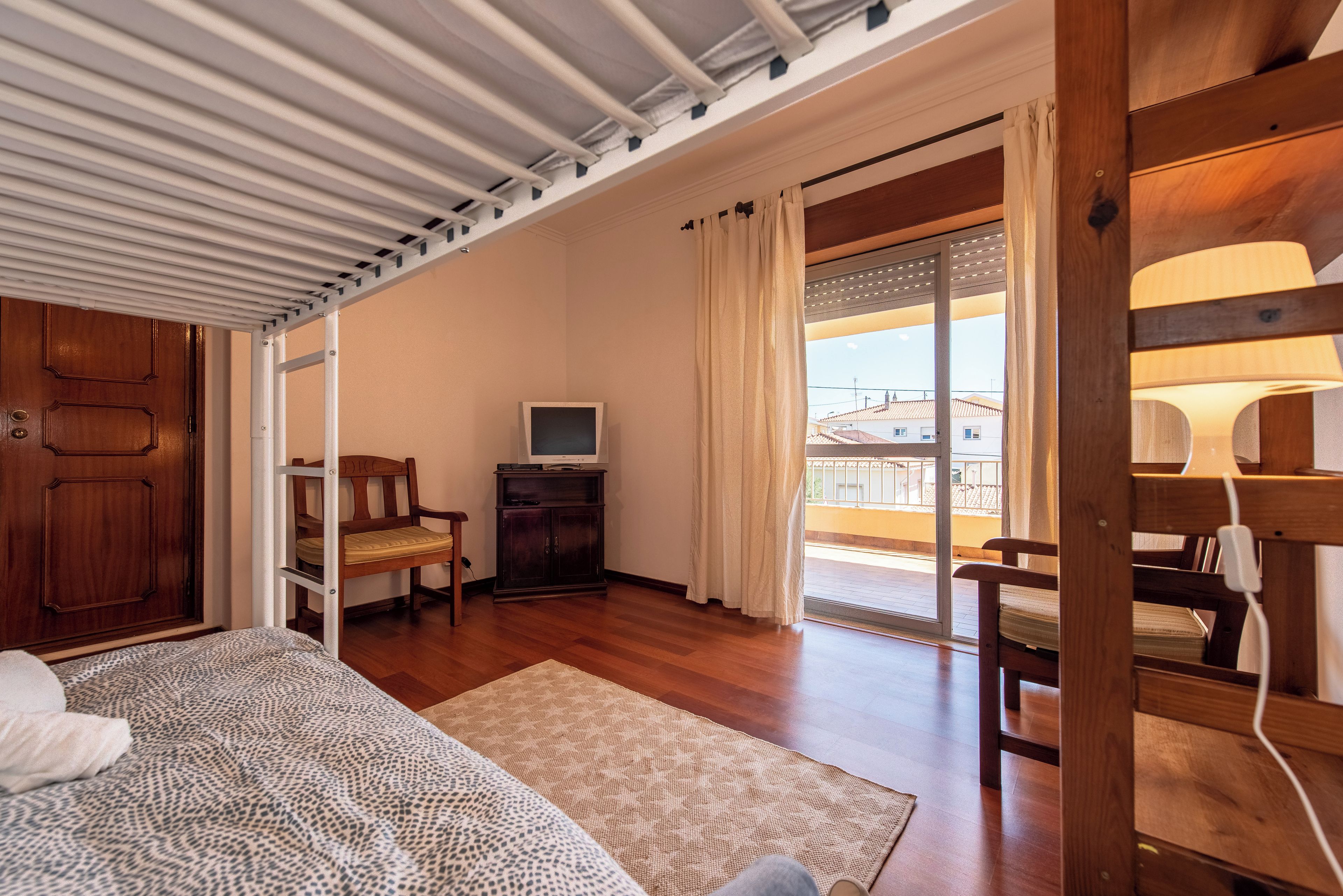 A bedroom with a bed, a wooden wardrobe, a television, a chair, and a balcony with a view.