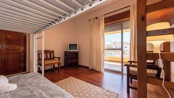 A bedroom with a bed, a wooden wardrobe, a television, a chair, and a balcony with a view.