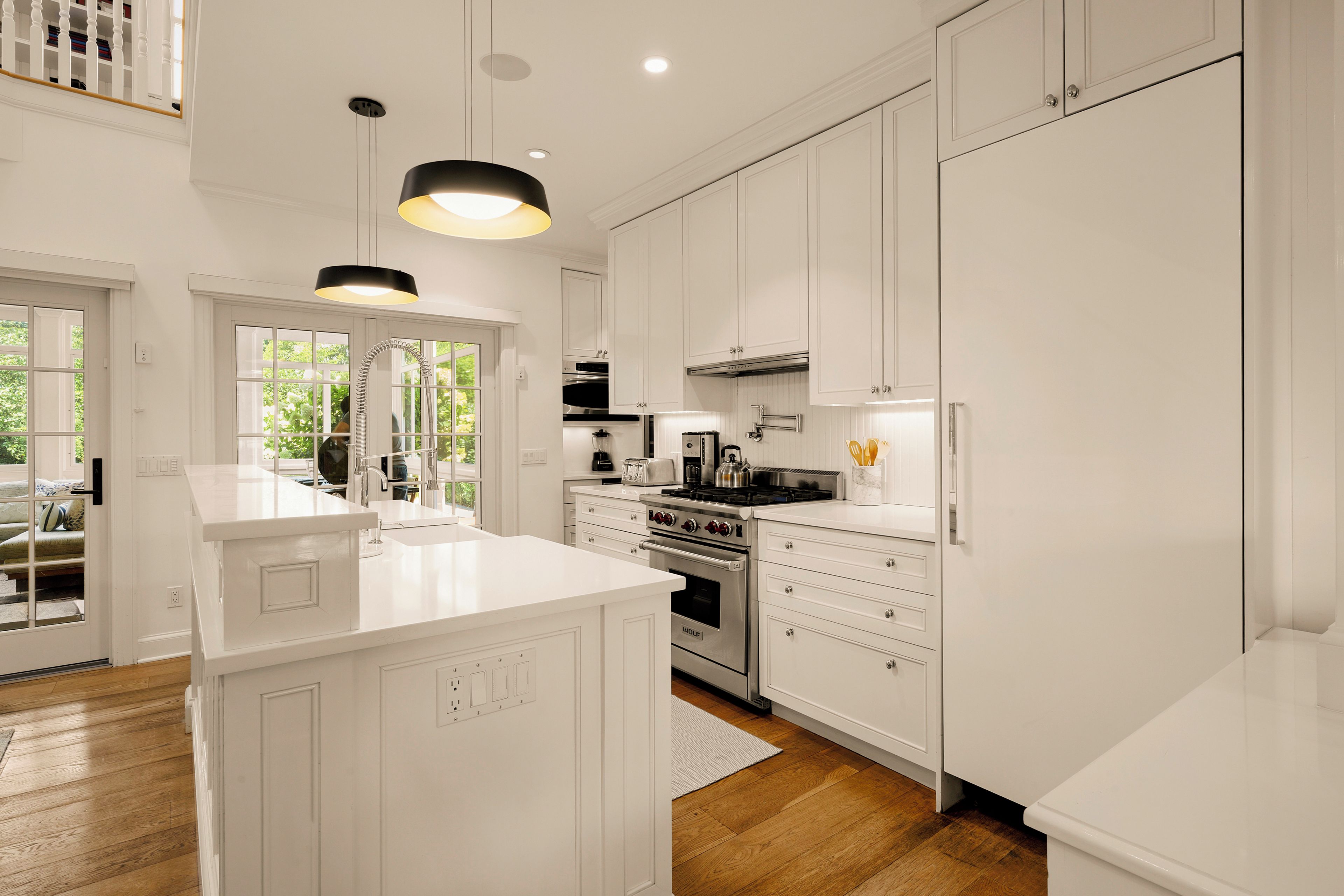 A modern kitchen with white cabinetry, a central island, stainless steel appliances, and pendant lighting.