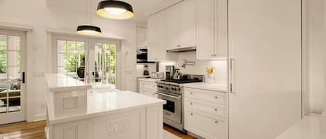A modern kitchen with white cabinetry, a central island, stainless steel appliances, and pendant lighting.