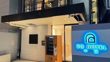 A hotel entrance with a neon sign, a vending machine, and a visible door.
