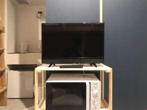 A television on a wooden stand with a microwave below it. - Riverside Hostel Yurariver Susaki (Fukuoka)