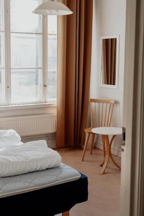Et hotelværelse med en seng, en stol, et bord og et vindue med gardiner.
