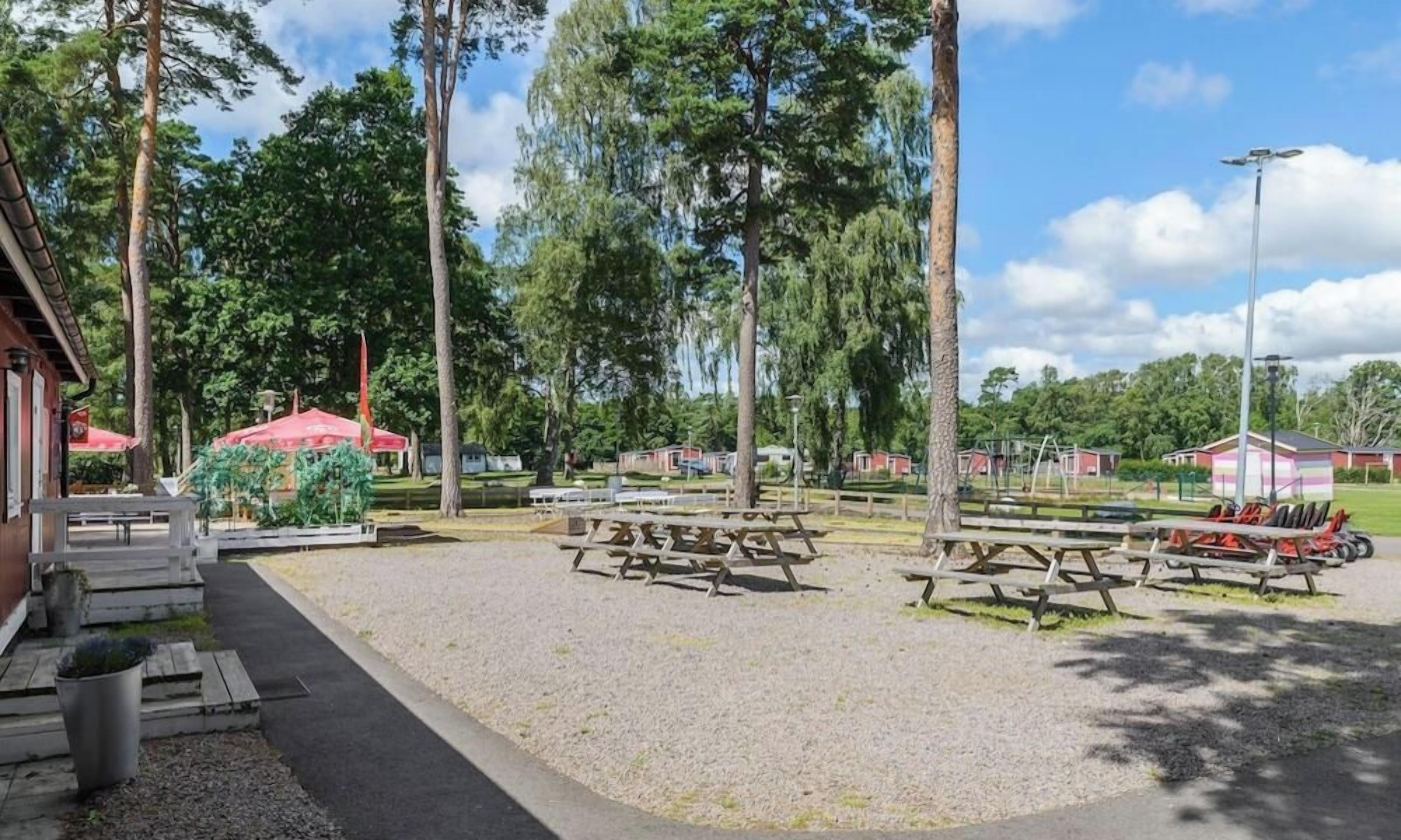 Een picknickplaats met tafels en banken, omringd door bomen en een gebouw met rode daken.