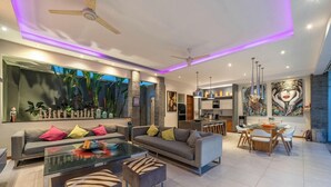 A modern living room with a sofa, coffee table, and chairs, a dining area with a table and chairs, and a kitchen in the background. - Villa Sawah (Seminyak)