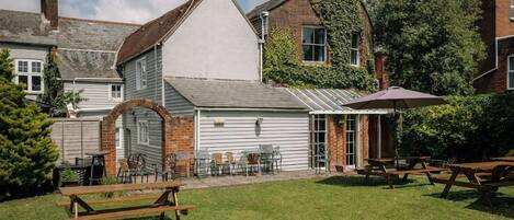 A courtyard with a brick building, a white structure with a sloped roof, and outdoor seating.