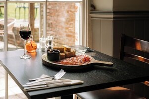 Una mesa de comedor con un plato de comida, una copa de vino tinto, saleros y pimenteros, y una botella de aceite de oliva.