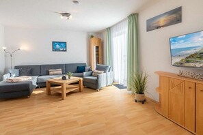 Ein modernes Wohnzimmer mit einer Sofagarnitur, einem Couchtisch, einem Schrank und einem großen Fenster mit Vorhängen.