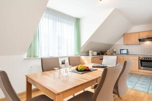 Eine moderne Küche mit Essbereich, mit einem Holztisch und Stühlen, einer Obstschale und einem Fenster mit Vorhängen.