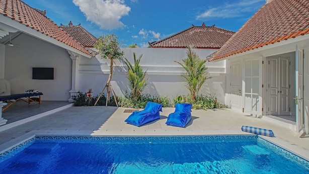 A swimming pool with two lounge chairs, a white building with a tiled roof, and a door. - Villaley Double Six (Legian)