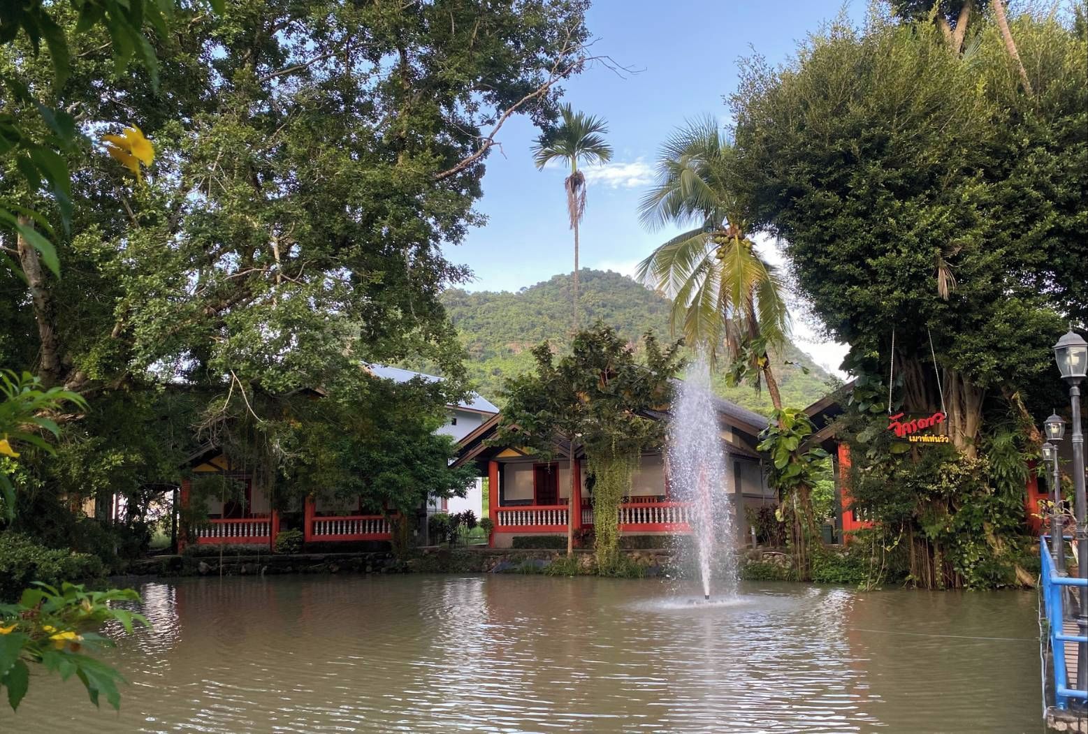 A traditional house with a water fountain in the foreground, surrounded by lush greenery and a clear sky.
